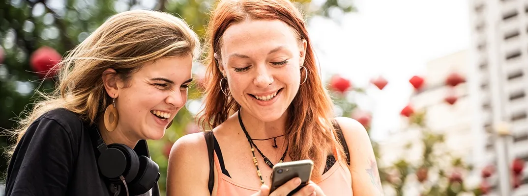 Two smiling women, outside, looking at a cellphone