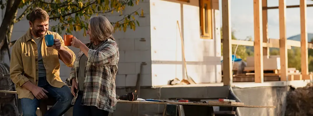 A man and a woman drinking coffee in front of a house under construction.