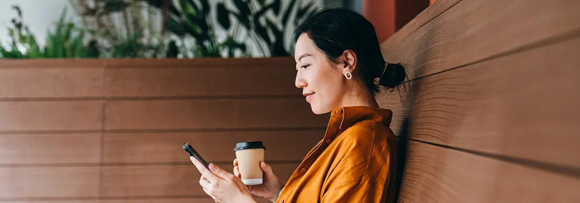 A woman sitting with her phone in one hand and a paper coffee cup in the other