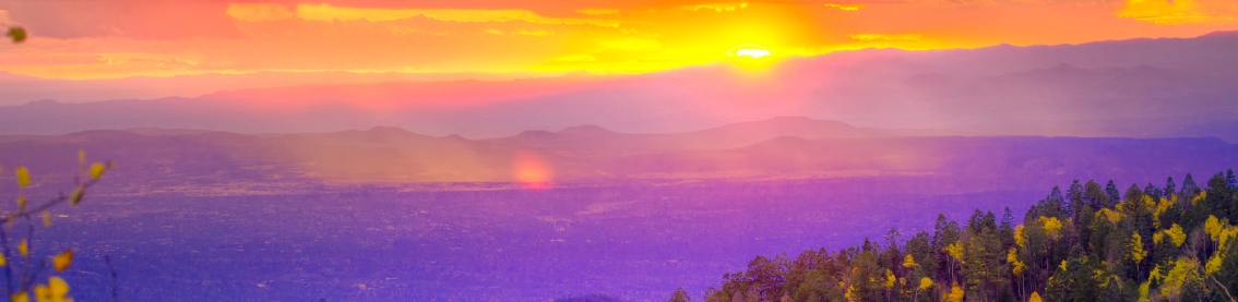 The sun peeking out from behind a mountain onto a landscape of wooded and mountainous terrain