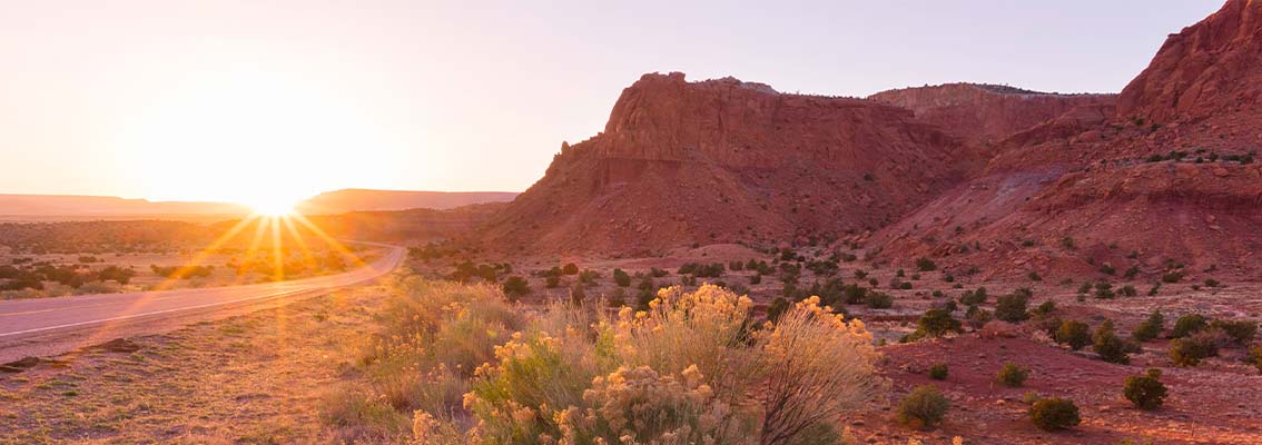 A desert landscape with the sun peeking over the horizon