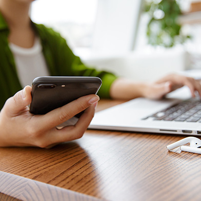 woman sitting in front of a laptop holding a mobile phone
