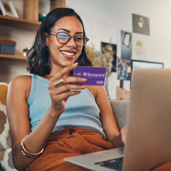 A woman with a laptop holding a Sunward Visa Signature Credit Card