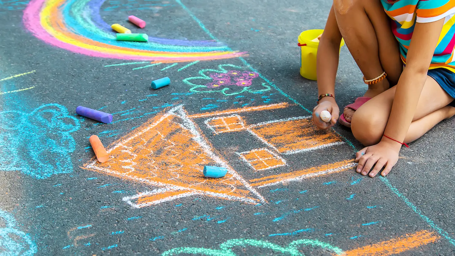 A child drawing a house with chalk on asphalt