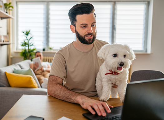 A man working on a laptop while holding a small dog